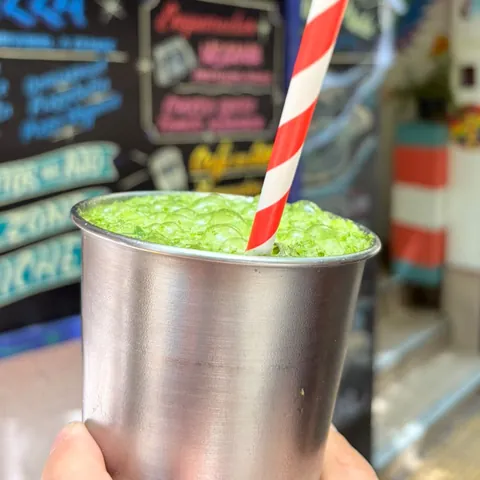 Limonada de menta en vaso metálico, con la pizarra del local de fondo