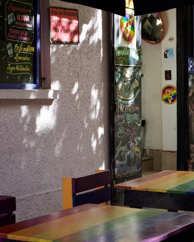 Mesas arcoíris en la entrada del local, junto a la pizarra de la carta