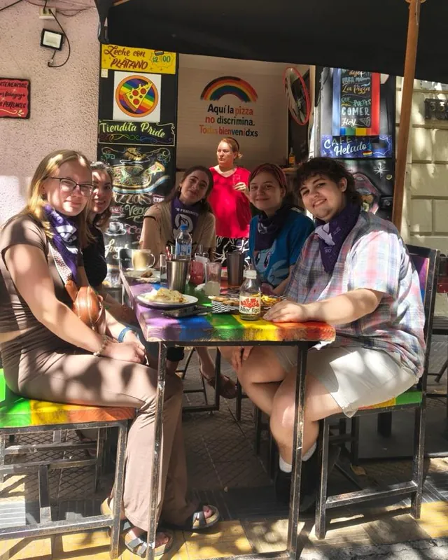 Grupo de personas en una mesa arcoíris de la terraza, con el muro del local de fondo