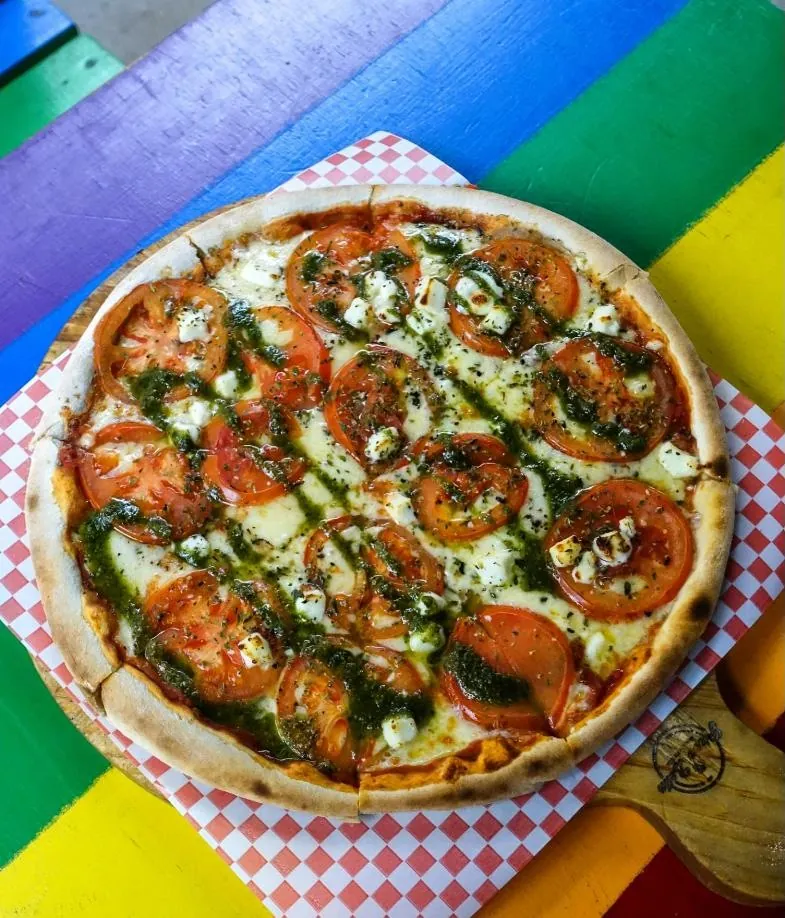 Pizza con rodajas de tomate, queso y pesto sobre una mesa arcoíris