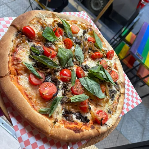 Pizza vegana con tomate cherry, champiñón, cebolla caramelizada y albahaca, en la terraza